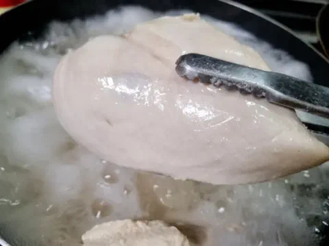 Pechuga de pollo hervida, recién retirada del agua con una pinza