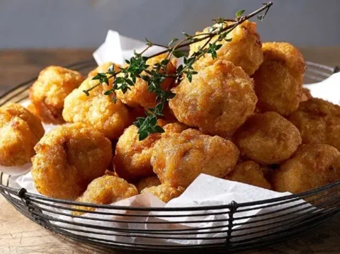 Bocados de pechuga de pollo estilo karaage, fritos y crocantes, servidos en una canasta con ramitas de tomillo
