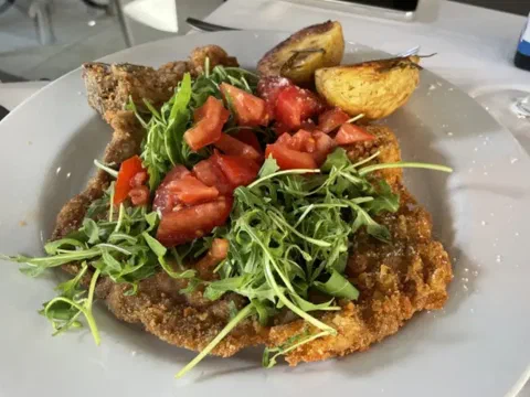 Pechuga de pollo a la milanesa, cubierta con ensalada de rúcula y tomate