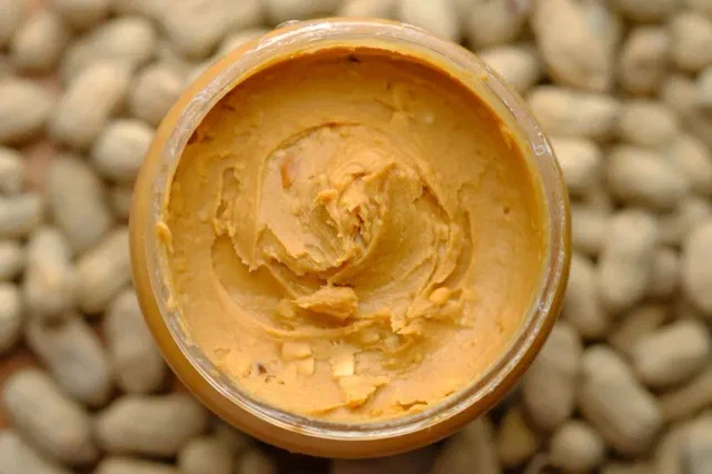 Mantequilla de maní en un frasco abierto, con maníes alrededor