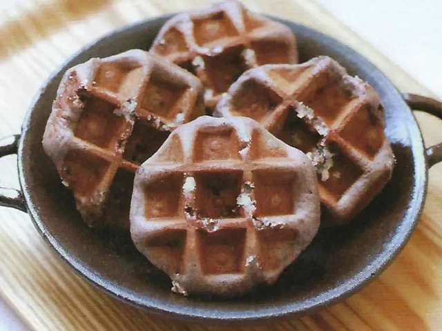 Waffles de Lieja oscuros de arroz negro, con azúcar perlada visible, en una sartén de hierro